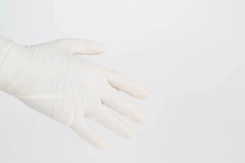 Hand in a white latex glove against a pale background
