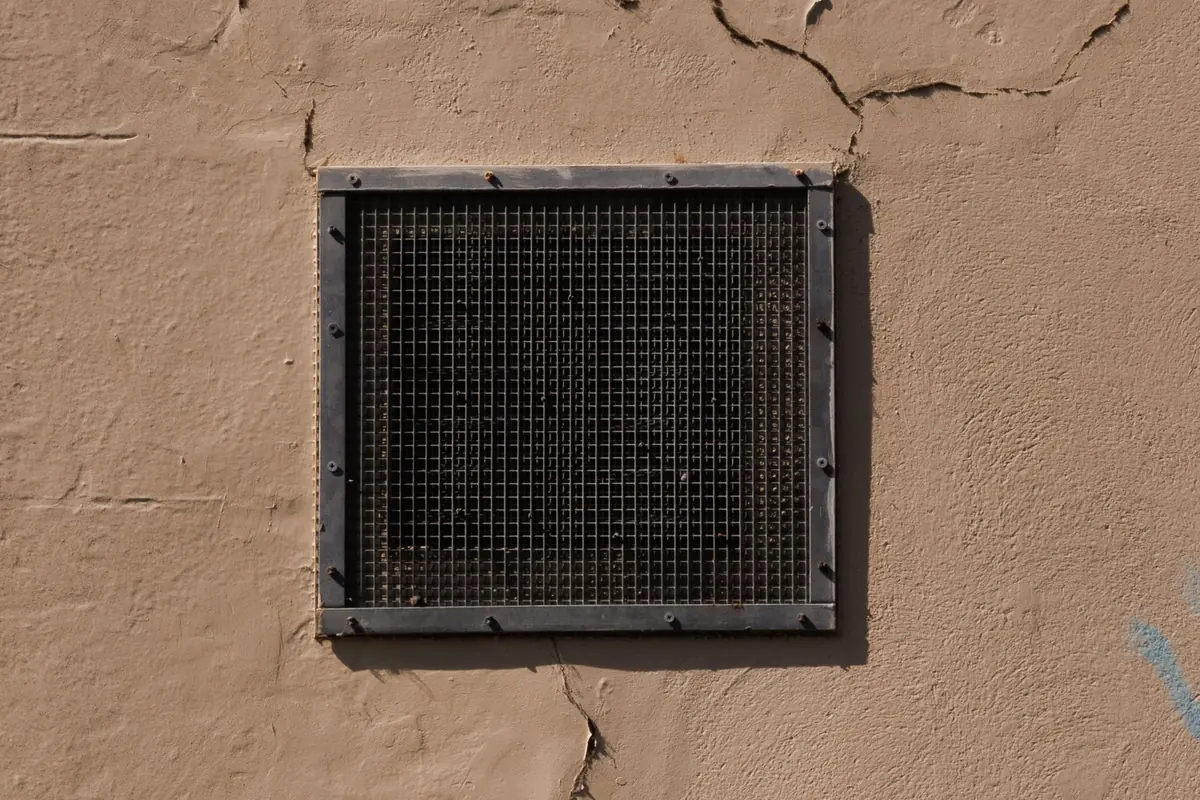 Metal vent grate set in a cracked exterior wall